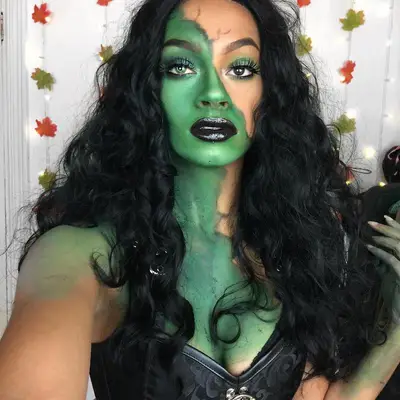 Makeup artist wears green goddess Halloween face paint look with glam eyeshadow and black lipstick