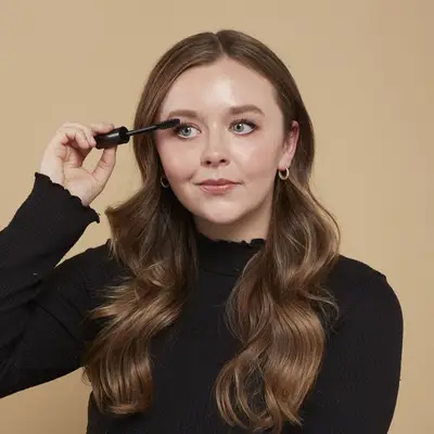 Woman applies mascara to her lashes