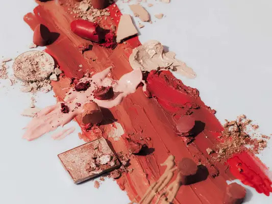 Studio photo of smashed lipsticks and other make-up products on white background.