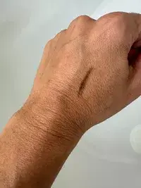 A line of Rare Beauty Brow Harmony Precision Eyebrow Pencil on the back of a hand on a white background