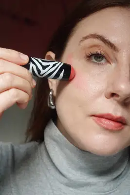 model is applying a stick cream blush to the cheek in an upward motion