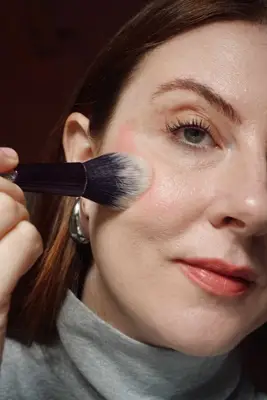 photo of model blending blush with a fluffy brush into the cheek