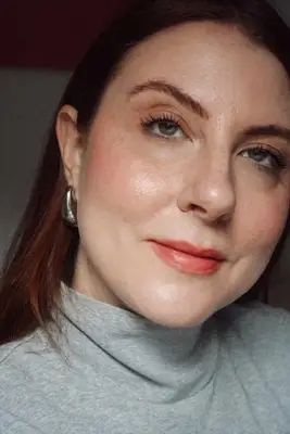 model is wearing a natural makeup look with a peach pink blush as the main focus