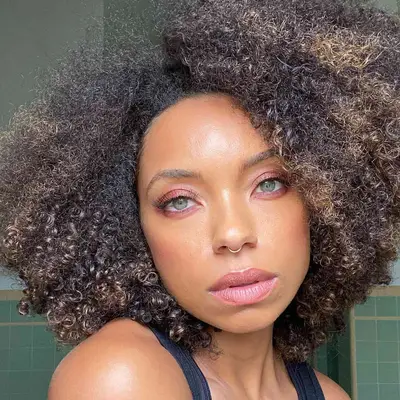 Logan Browning wears rosy pink eyeshadow, mascara, and pink lipstick