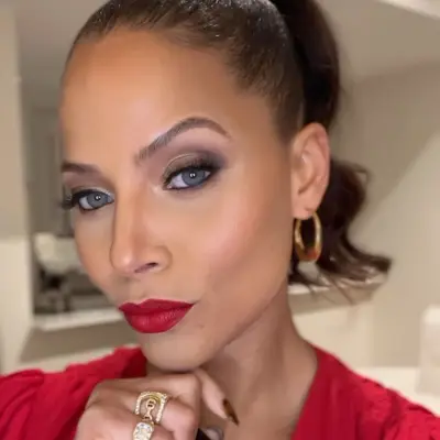 Denise Vasi wears smoky eyeshadow, red lipstick, and a ponytail hairstyle