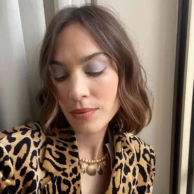 Alexa Chung wears gray eyeshadow, rosy neutral lipstick, and a leopard print shirt with a shell necklace