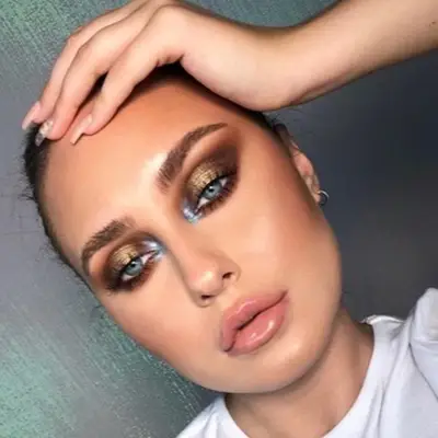 Woman with bronze and blue eyeshadow look, blue eyes, and glossy lips