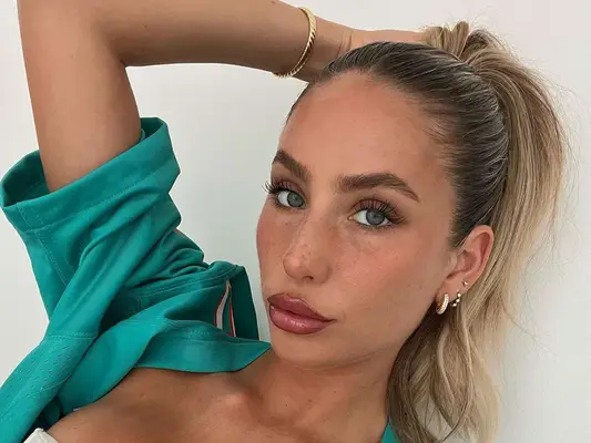 Alix Earle wears brown eyeshadow, mascara, a ponytail hairstyle, and glossy lips with brown liner