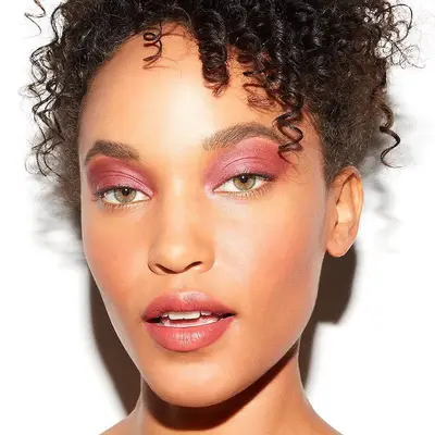 Model with fiery pink eyeshadow, green eyes, warm-toned blush, and berry pink lipstick