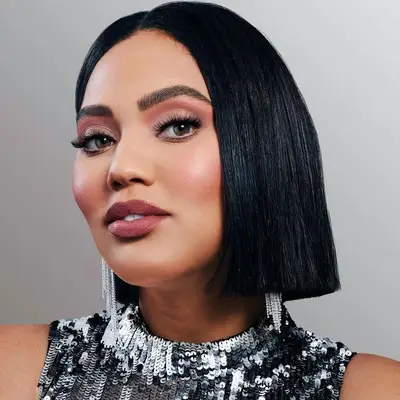 Ayesha Curry wears warm-toned eyeshadow, dramatic lashes, berry-toned lipstick, and blush