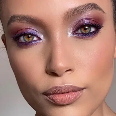 Model with shimmery purple eyeshadow, green eyes, blush, and neutral lipstick