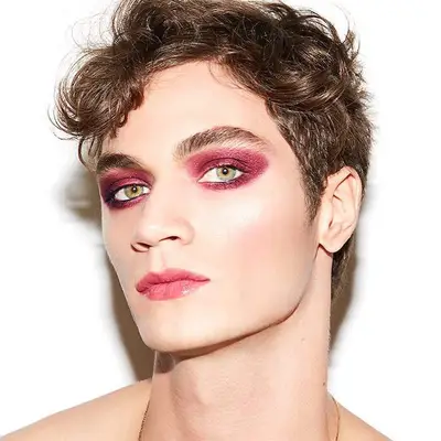 Model with warm-toned purple eyeshadow, green eyes, berry lipstick, and subtle blush