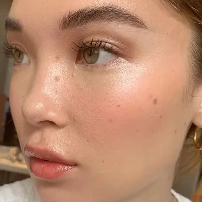 Woman with dewy skin, champagne shimmer eyeshadow, green eyes, and glossy lips