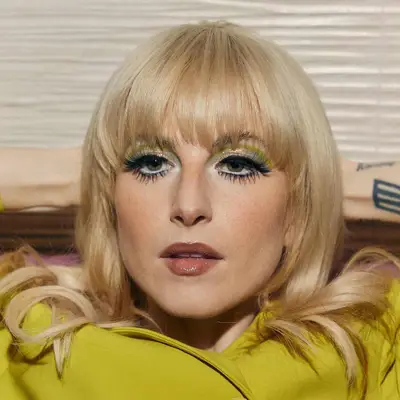 Hayley Williams with dramatic Twiggy lashes, green and gold graphic eyeshadow, green eyes, subtle blush, and a glossy rose lip