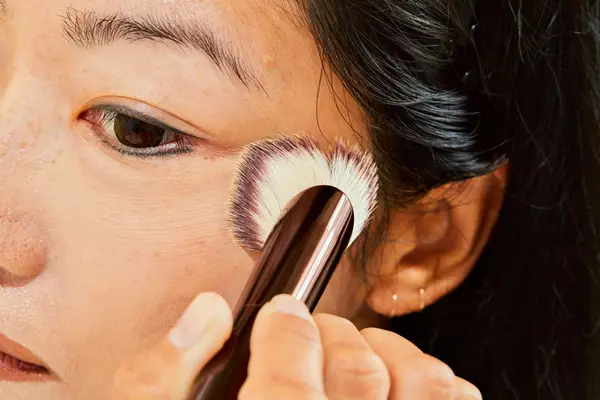 Close-up of a person using a Hourglass Ambient Soft Glow Foundation Brush on their face