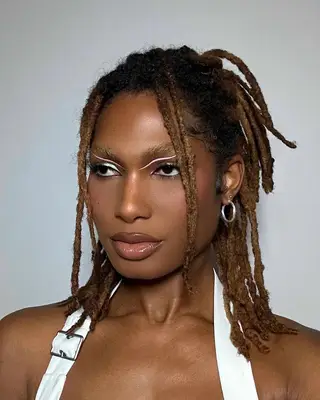 Shaqori Morris, a Black trans woman, showing off her makeup with abstract pink eyeliner, glossy lips, and bleached eyebrows. She is wearing silver jewelry and a white halter top.