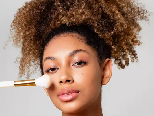 A woman with curly hair is holding a makeup brush 