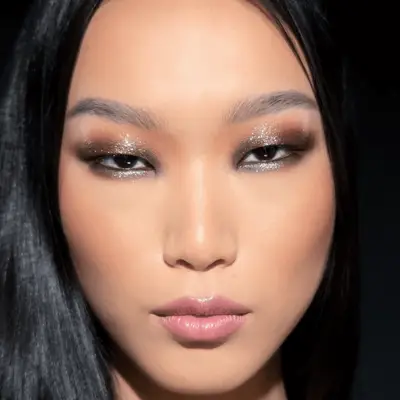 model wears a faint copper shadow with dramatic black eyeliner applied around the eye