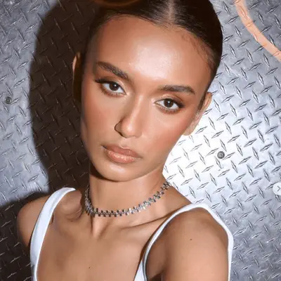 model wears copper eyeshadow with a thick black liner and false eyelashes, paired with dewy skin and glossy lip