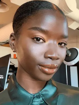 Model with dark skin wears shimmery copper eyeshadow and deep berry glossy lipstick