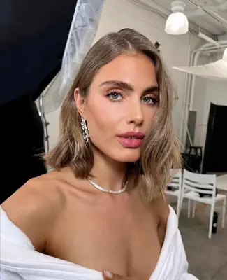 model wears a makeup look consisting of bold brows, lashes, and pink lipstick with soft, contoured and sculpted skin