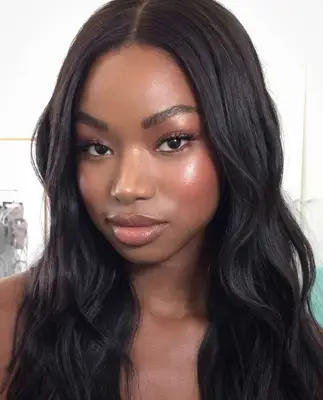 model wears natural makeup that consists of a glowing complexion with highlighter on the cheeks and browbone, peachy pink blush and lips