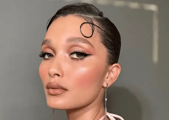 A model with slicked back hair, shimmery eyeshadow, and rose colored blush