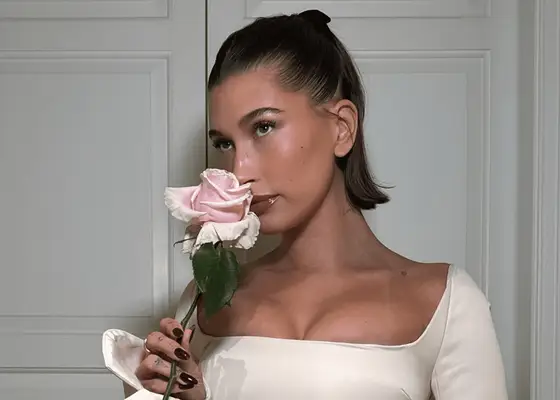 hailey bieber wearing baby pink blush while sniffing flower