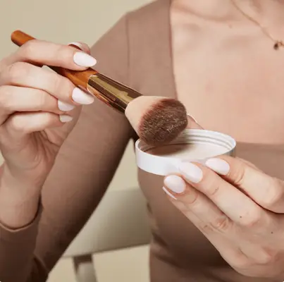 woman tapping makeup brush on powder lid