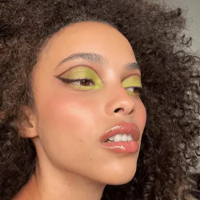 A model with long curly hair wearing green and purple eyeshadow