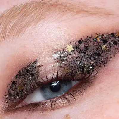 Close-up of eye with charcoal glitter eye makeup with gold stars