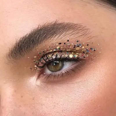 Close-up of eye with gold sequins and various colored flecks on eyelid