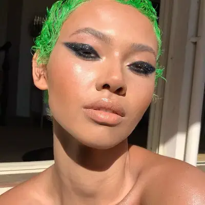 Model with green pixie cut, black glitter graphic eye makeup, and radiant skin