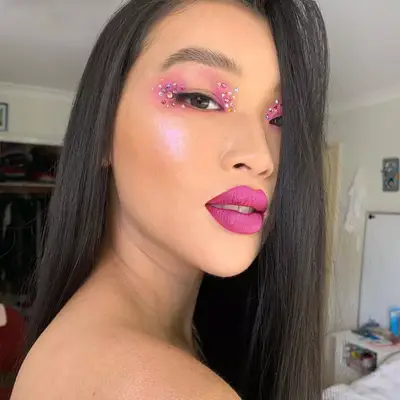 Model with monochromatic pink eyeshadow, blush, and lipstick and multicolored eye gems