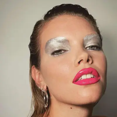 Silver eyeshadow look that completely covers the brows with hot pink lipstick.