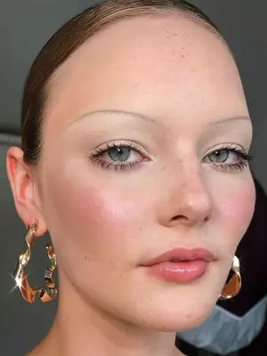 model wearing thin brows and spidery lashes and pink lip gloss