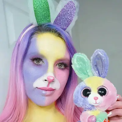 Creator wears a purple, yellow, and pink Beanie Baby bunny makeup look with ears and colored hair