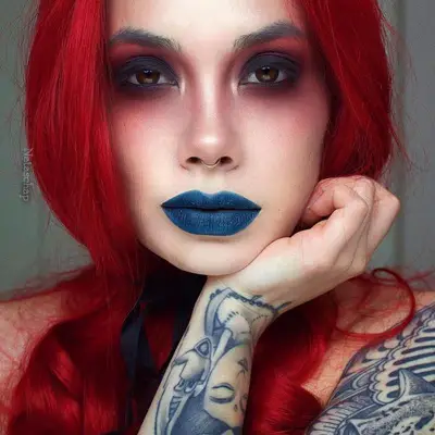 Makeup artist with red and black smoky eye makeup and blue lipstick