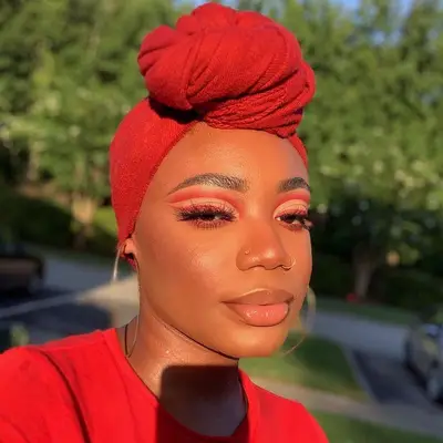 Woman with red graphic eye makeup, head wrap, and neutral glossy lips