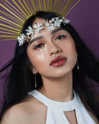 Beauty creator wears a gold headpiece and gold glitter tears