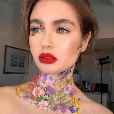 Makeup look with bold red lip and flowers attached to the eye and neck