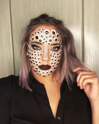 Makeup artist wears face covered in googly eyes and burgundy lipstick