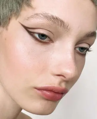 model wears abstract winged eyeliner in chocolate brown shade extending outward from the outer corner of the eye