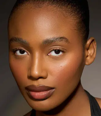 model wears a natural makeup look with rosy blush and glossy nude lips
