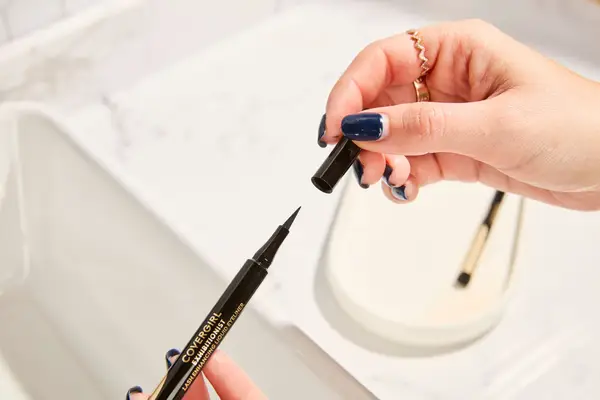 Hands hold a COVERGIRL Exhibitionist Lash Enhancing Liquid Eyeliner