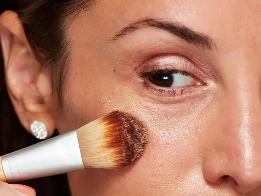 Close up of a woman with mature skin applying concealer under her eyes