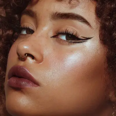 Model with a berry lip, radiant skin, and graphic double winged eyeliner