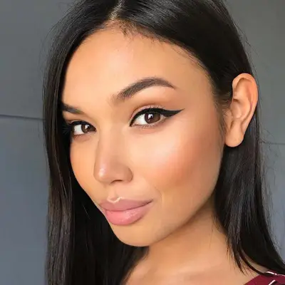 Model wears simple makeup look with warm blush and cat eye liner