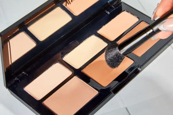A person applies the KVD Beauty Shade + Light Powder Face Contour Palette