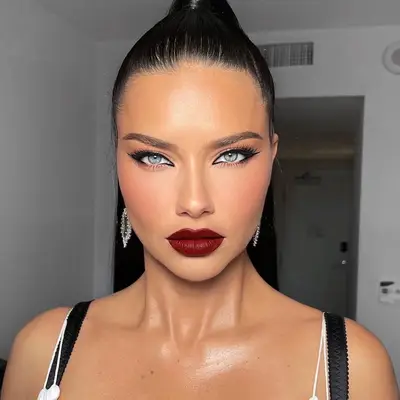 Adriana Lima wears sharp black eyeliner, blended blush and highlight, and burgundy lipstick